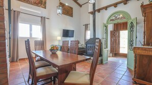 A dining area with a wooden table and chairs, a television mounted on the wall, and a fireplace. - La Era del Bonete Constantina by Ruralidays (Sevilla)
