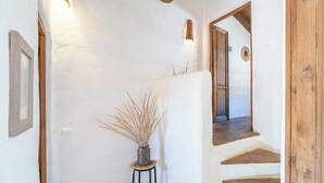 Un pasillo con una puerta de madera rústica, una mesa pequeña con un jarrón de plantas secas y una lámpara en la pared.