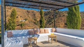 Una terraza en la azotea con un sofá blanco, dos mesas de madera y una pérgola.