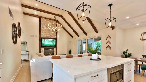 A modern kitchen with a large island, wooden beams, and pendant lighting.