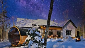 A cabin with a large cylindrical window, a snow-covered tree, and a starry night sky.