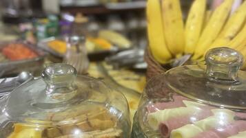 Un bufé con diversos alimentos bajo campanas, incluyendo pasteles y plátanos.