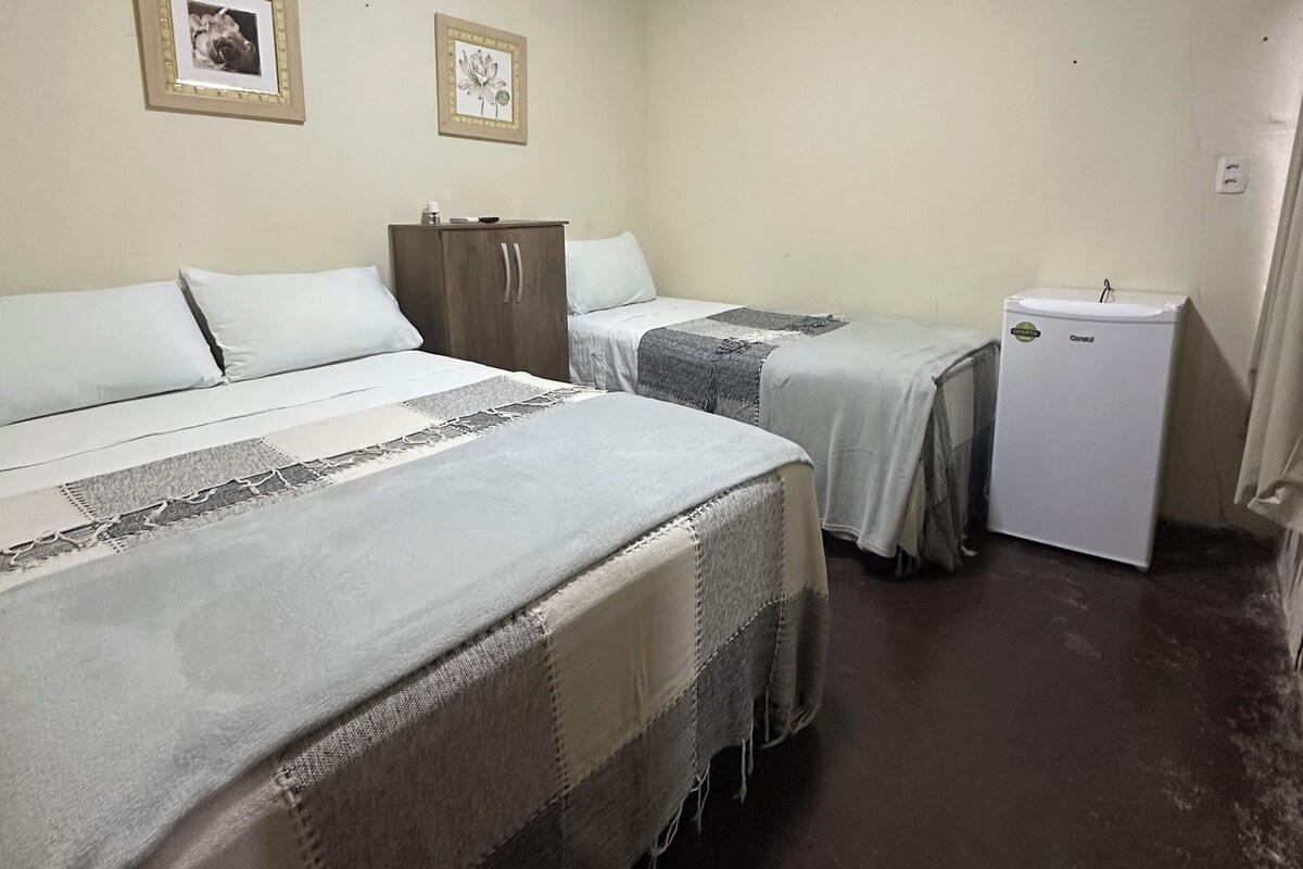 Una habitación pequeña y limpia con dos camas, un armario pequeño y un refrigerador.