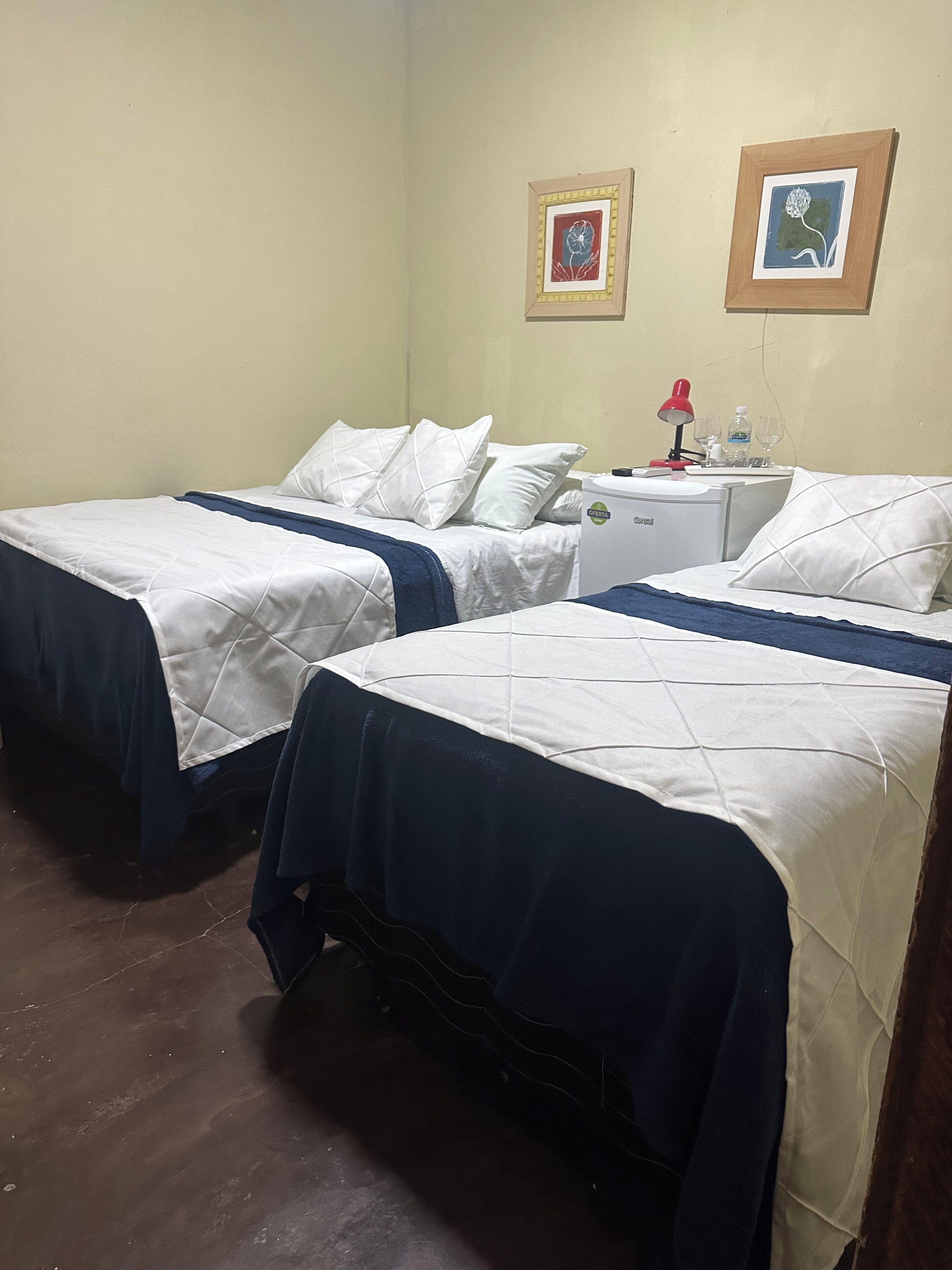 Camera d'albergo con due letti singoli, una piccola scrivania con una lampada e due quadri appesi al muro.