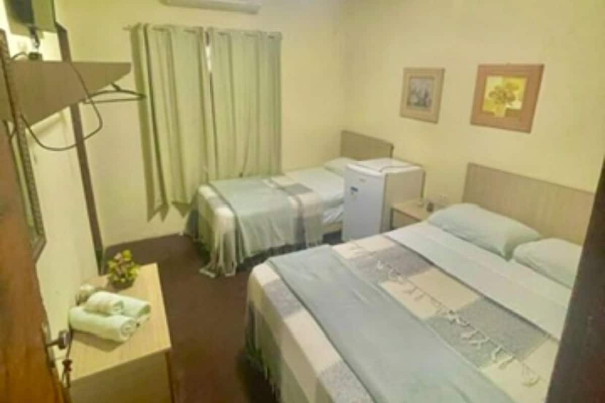 A hotel room with two beds, a desk, an air conditioning unit, and a small table with a towel.