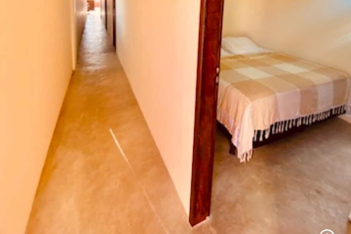 A narrow hallway with a bed at the end, an air conditioning unit on the wall, and a tiled floor.