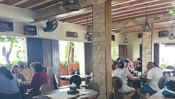 A restaurant with wooden tables and chairs, stone pillars, and hanging light fixtures. - Pousada Berro do Bode (Cabaceiras)