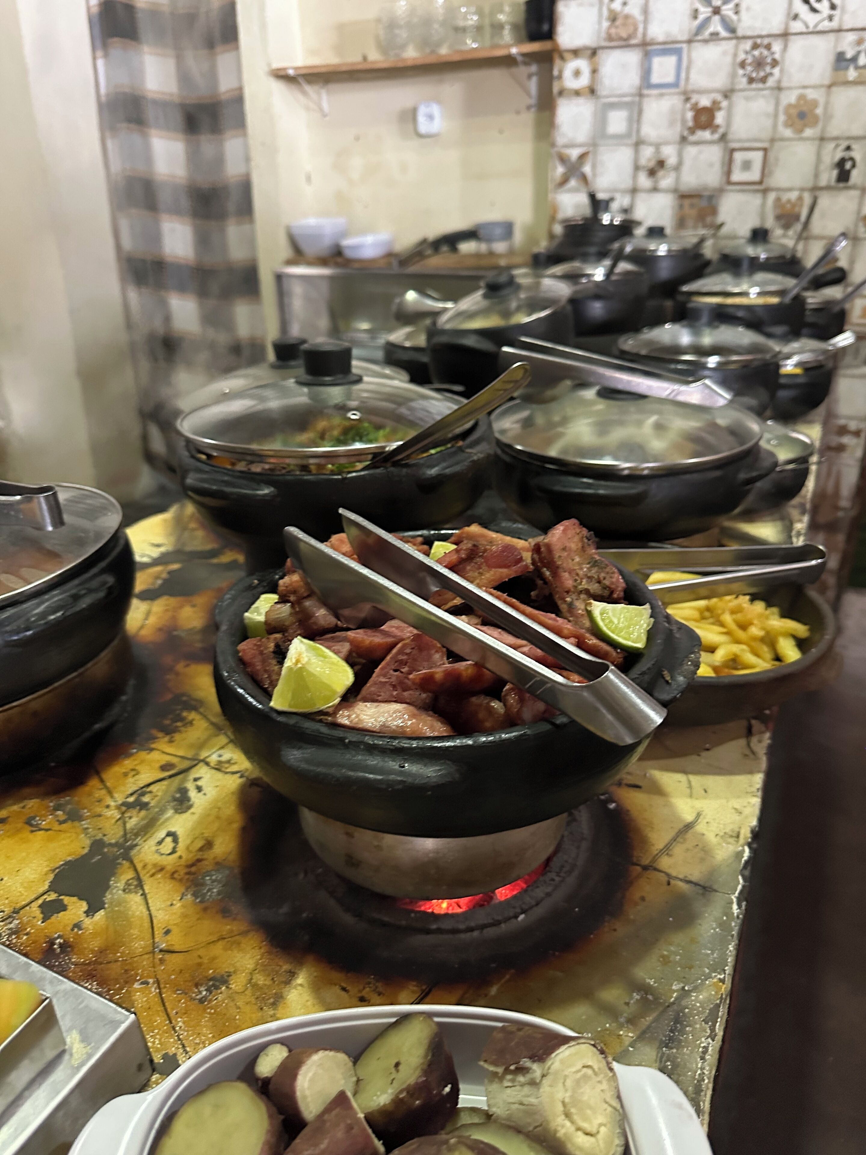 Una cocina con varias ollas en la estufa, un tazón de carne con limón y un plato de papas rebanadas.
