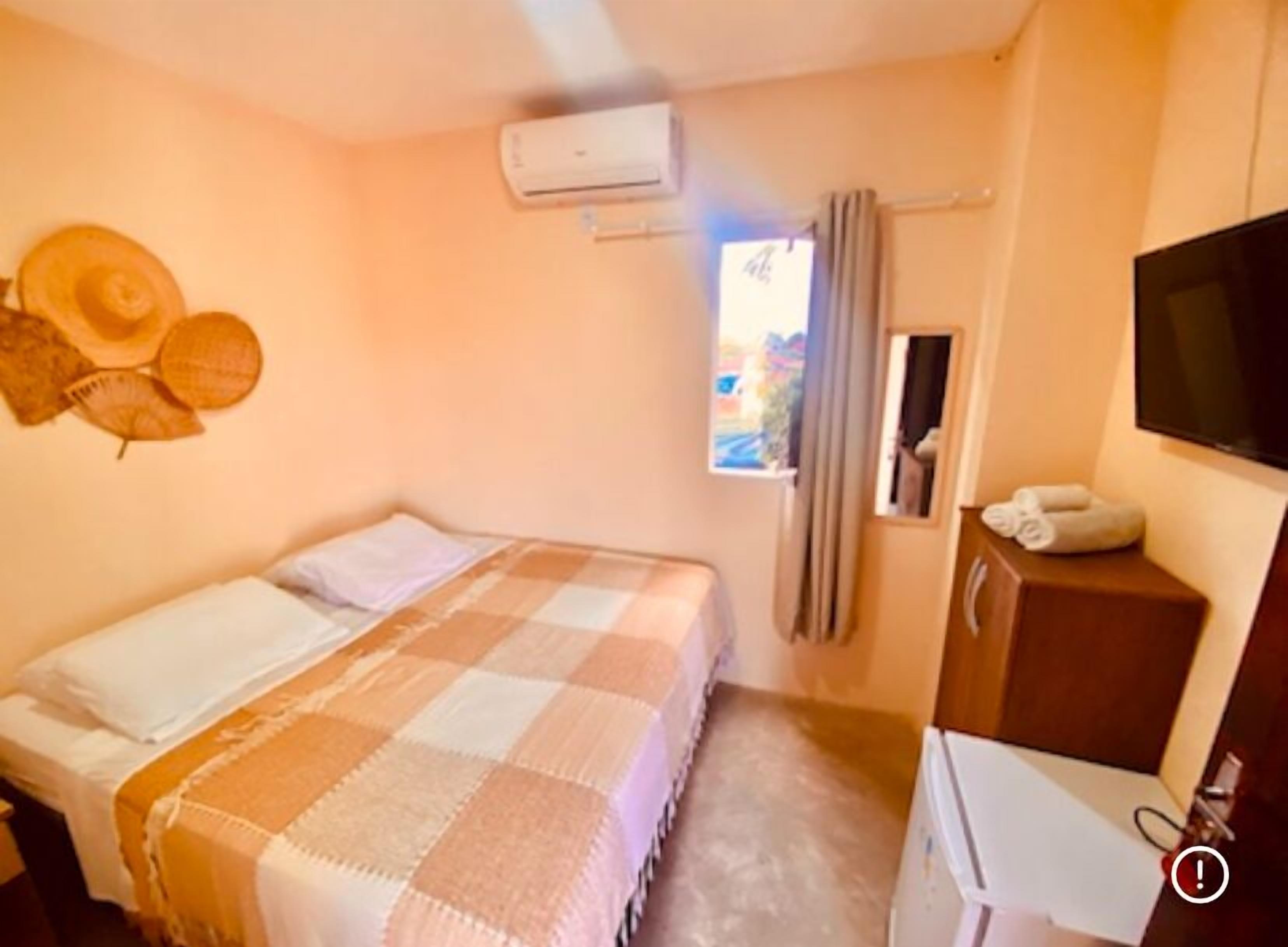 A hotel room with a bed, a TV, a desk, and an air conditioning unit.
