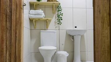 Un baño con inodoro, lavabo y estante con toallas y una planta pequeña.