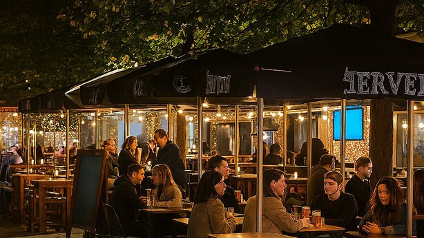 Un cafè a l'exterior amb taules i cadires sota una marquesina, envoltat d'arbres.