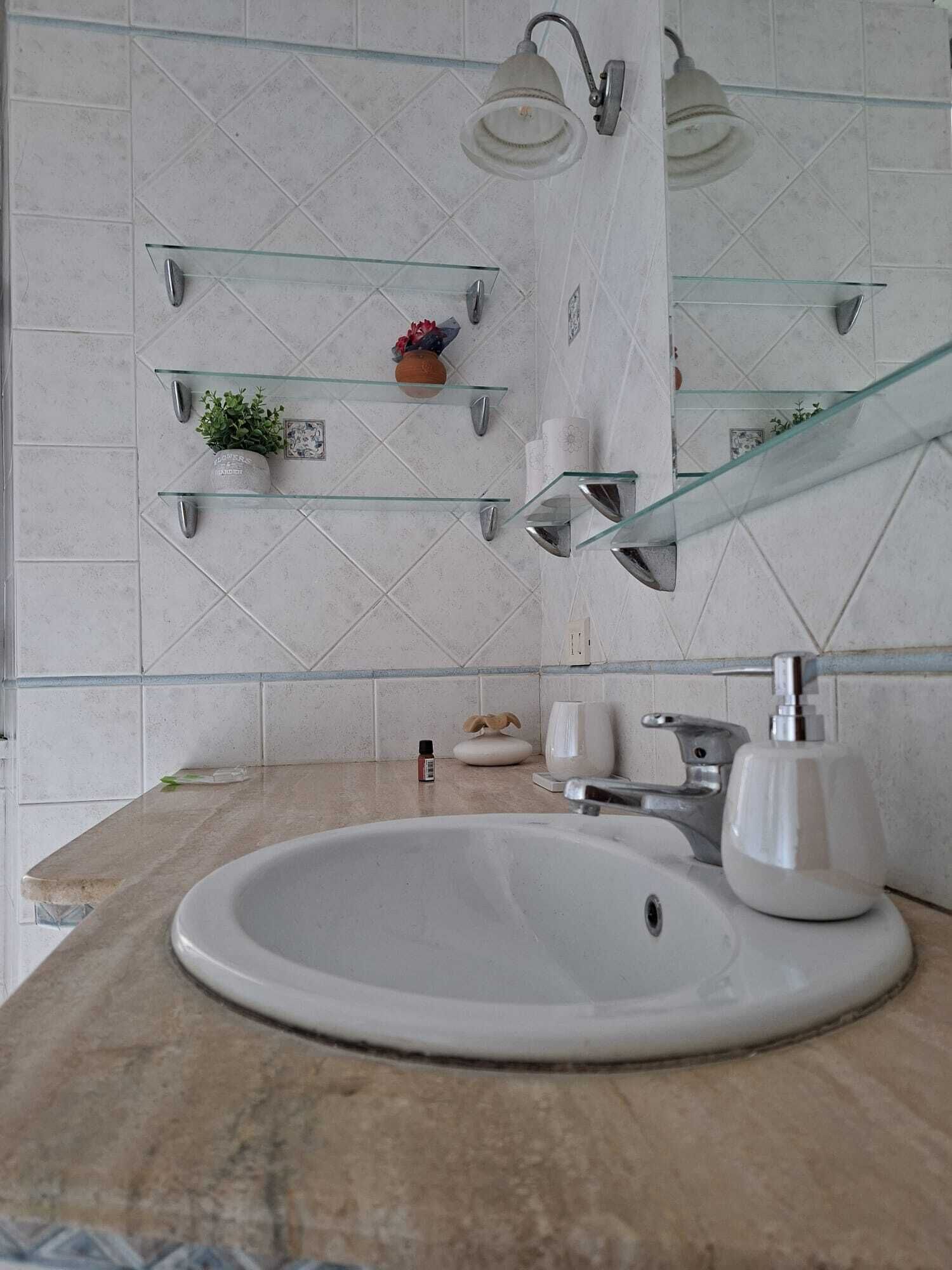 A bathroom with a white sink, glass shelves, and a mirror.