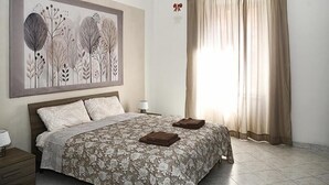 Un dormitori amb un llit, una tauleta de nit, una làmpada, una obra d'art engretada gran i una finestra amb cortines.