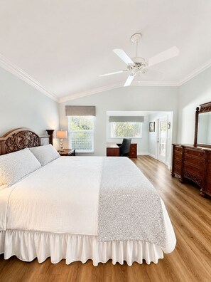 Un dormitorio con una cama grande, ventilador de techo, escritorio y cómoda.