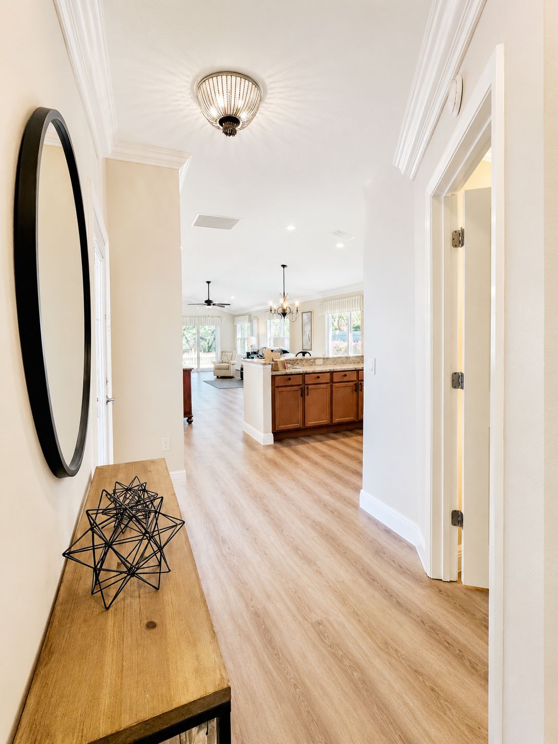 Una cocina moderna con armarios de madera y una isla central, un comedor con mesa de madera, y un pasillo con un espejo grande y una araña.