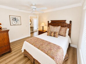 A bedroom with a large bed, a wooden headboard, a nightstand with a lamp, a dresser, and a ceiling fan. - Sunshine Stay a Creekside Villa at Lake Sumter Landing with Nature & Water Views (The Villages)
