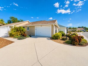A single-story house with a garage, surrounded by landscaped gardens and a clear blue sky. - Sunshine Stay a Creekside Villa at Lake Sumter Landing with Nature & Water Views (The Villages)