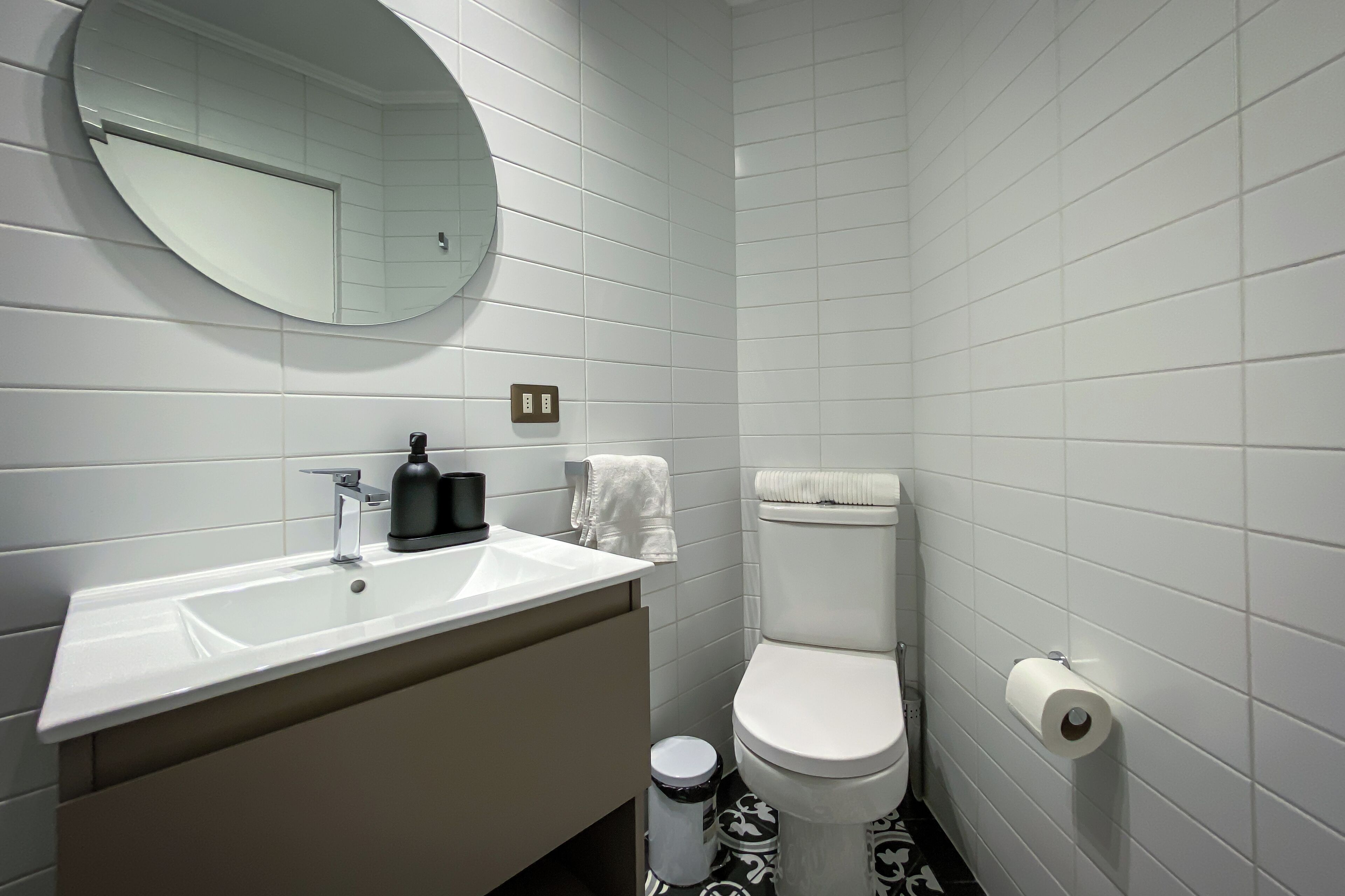 Un baño con lavamanos blanco, espejo, inodoro y un cesto de basura.