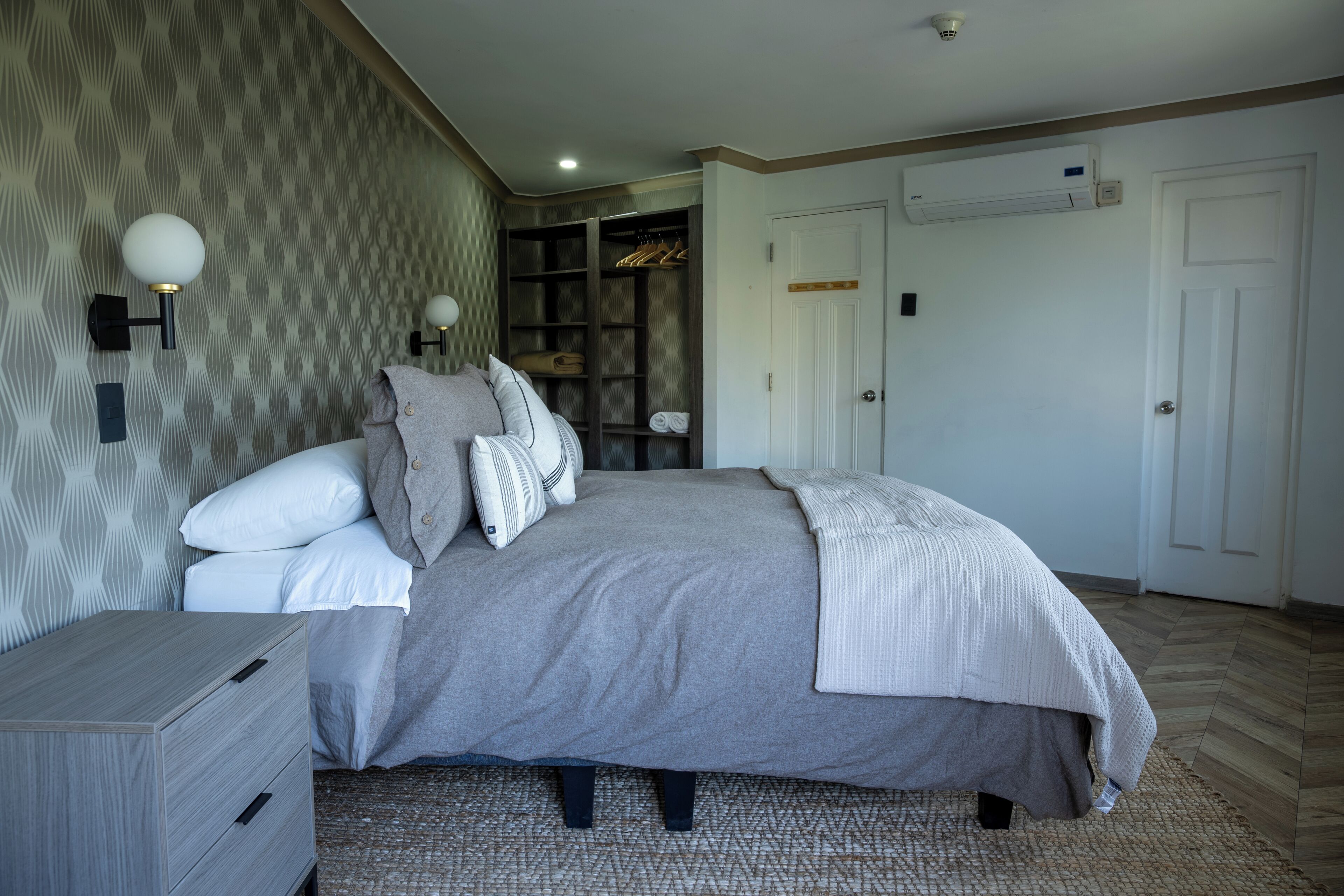 A bedroom with a bed, a nightstand, a wardrobe, and an air conditioning unit.