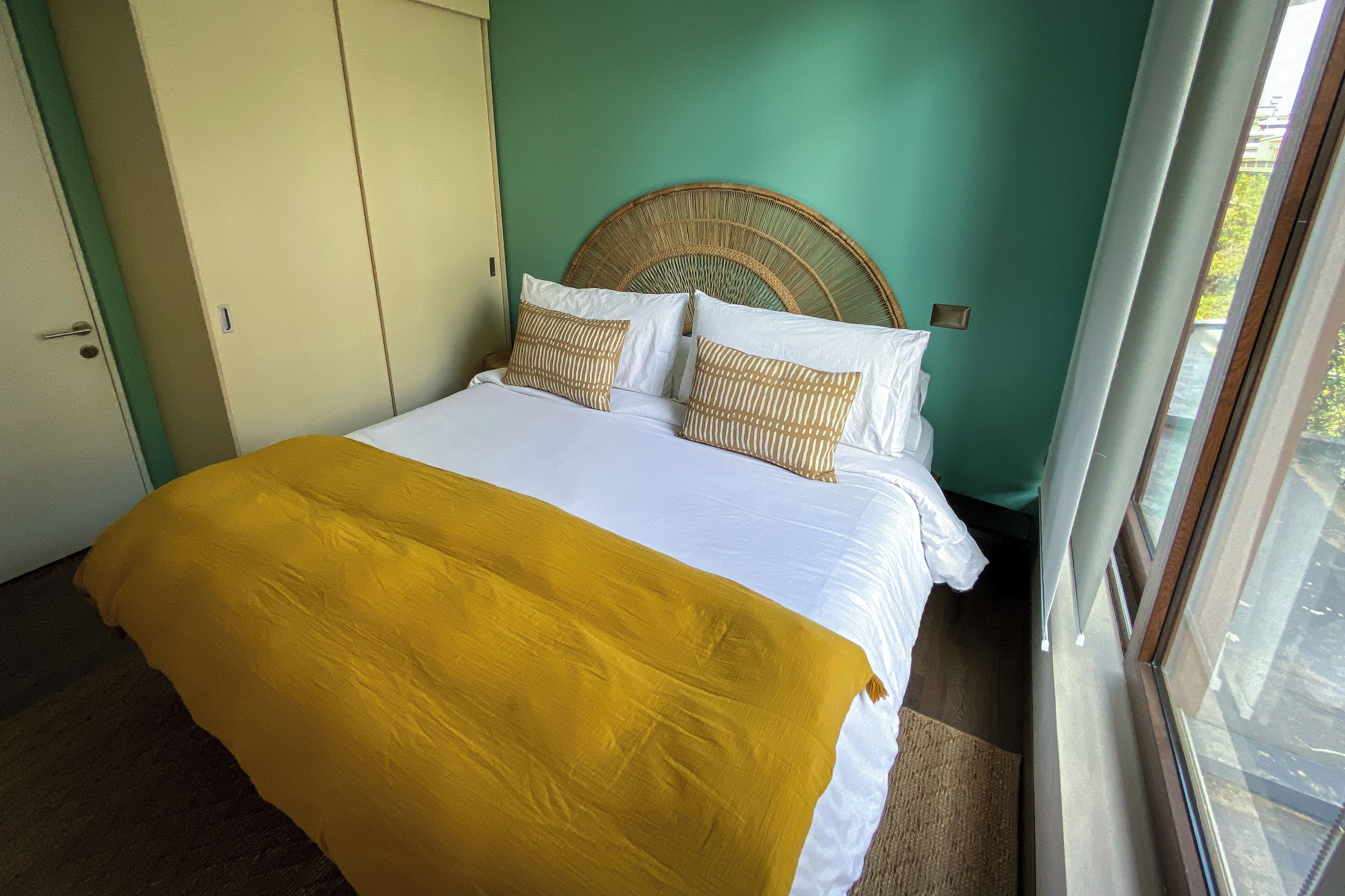 A bed with a yellow blanket, white pillows, and a woven headboard.