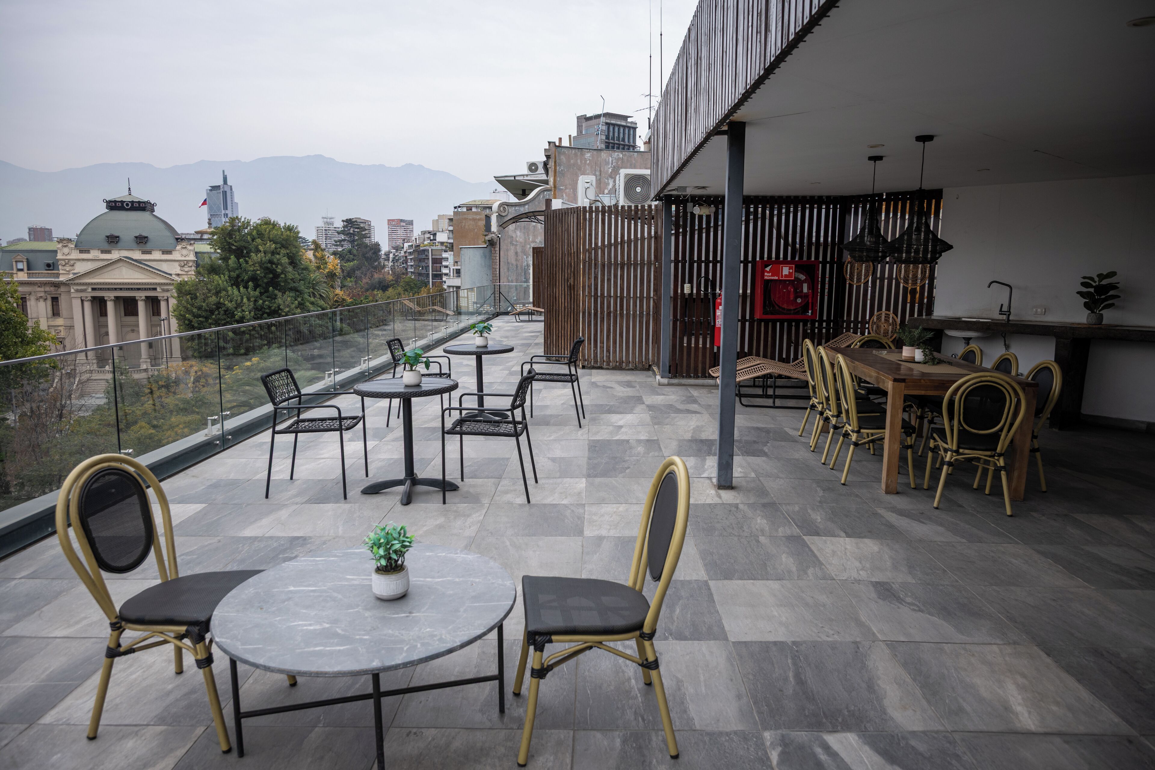 Terraza en la azotea con zona de comedor, mobiliario exterior y vistas a edificios de la ciudad y montañas.