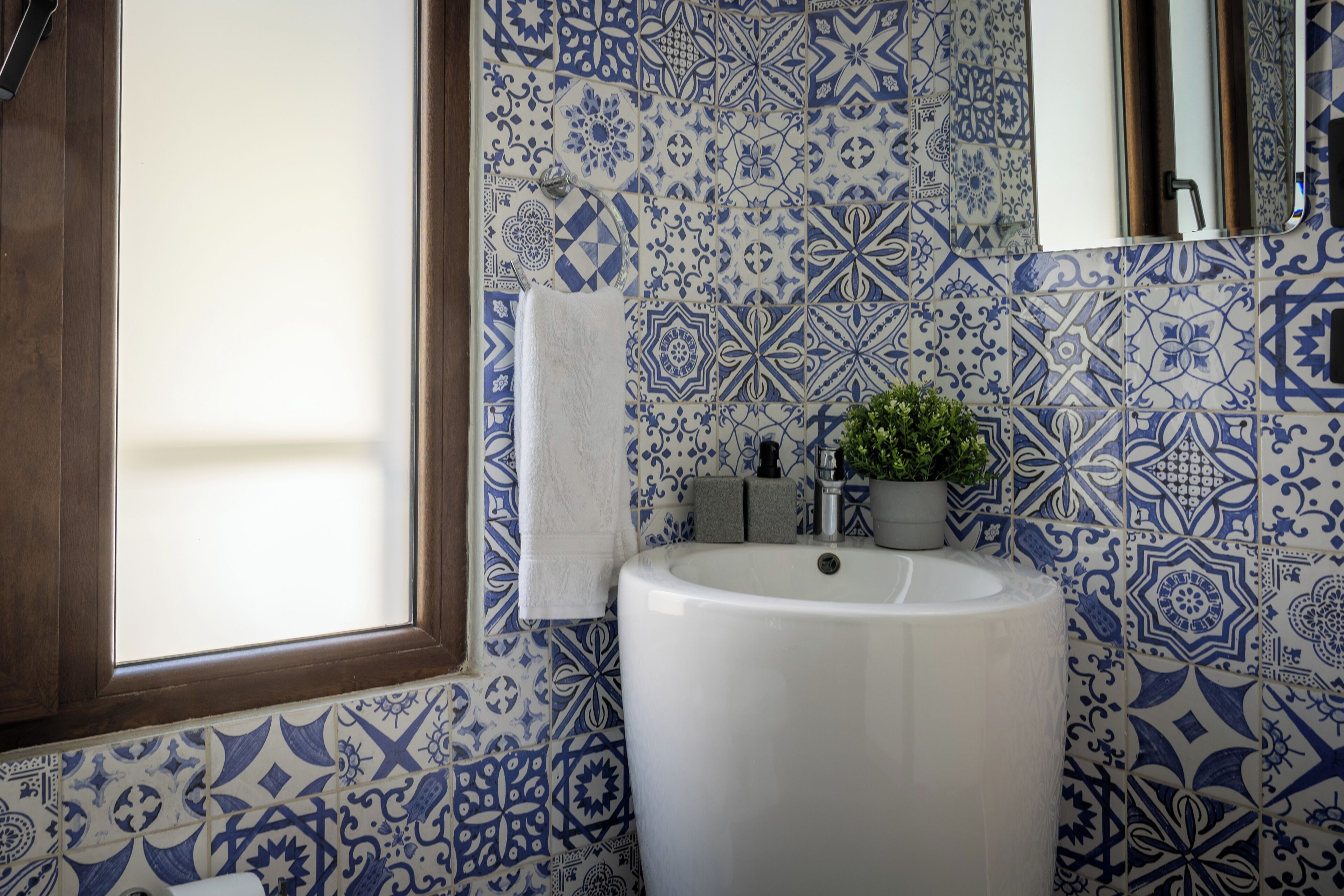 Un baño con un lavamanos blanco, azulejos estampados en azul, un ventanal y una toalla colgada en la pared.
