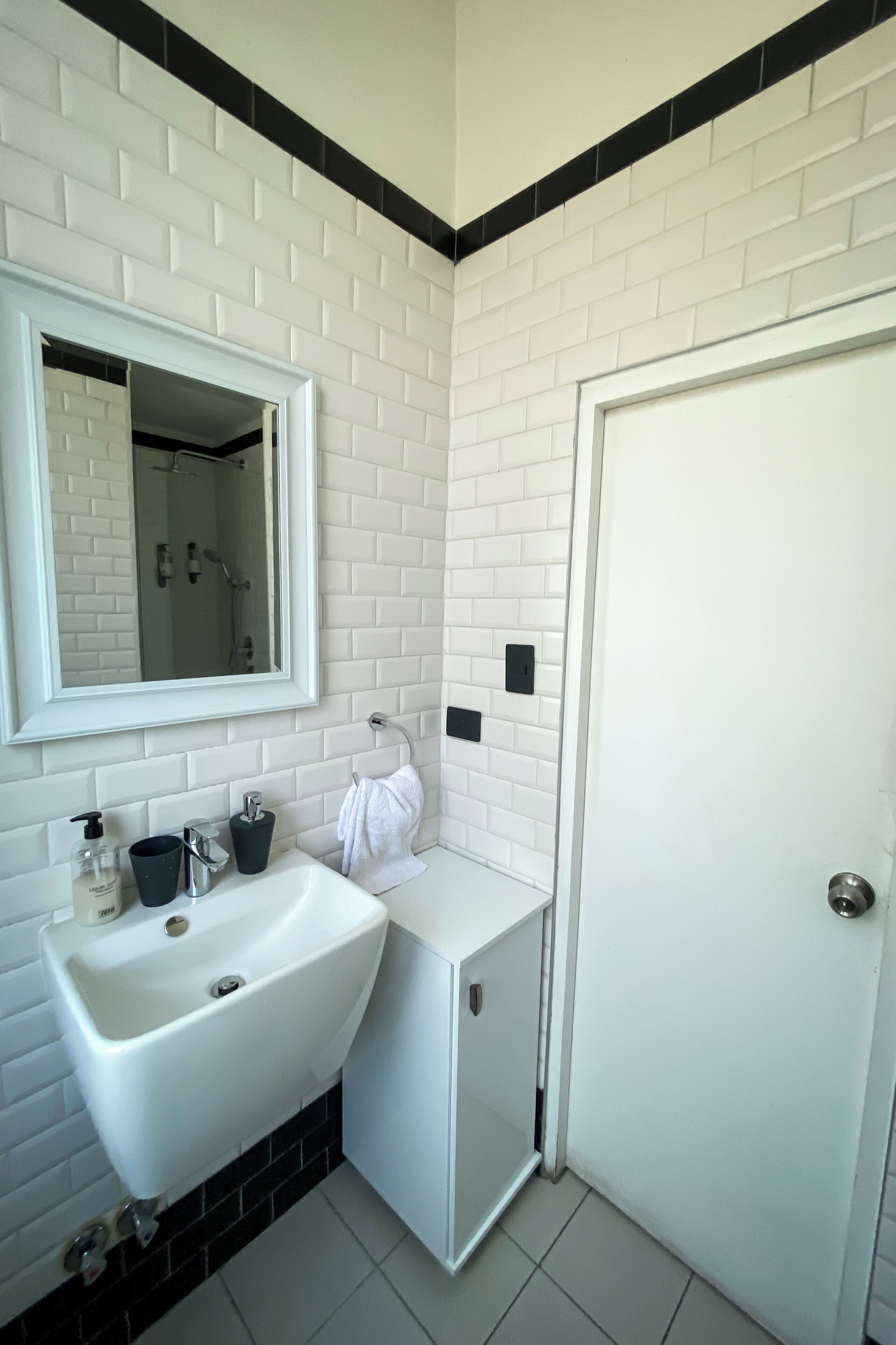 Un baño con lavamanos, espejo y puerta blancos.