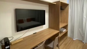Una habitación de hotel moderna con un escritorio de madera, un televisor de pantalla plana, una cama con almohadas rojas y una cortina blanca.