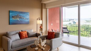 Ein Wohnzimmer mit grauem Sofa, einem Couchtisch mit Dekoration, einem Walbild und einem Balkon mit Blick auf die Stadt.