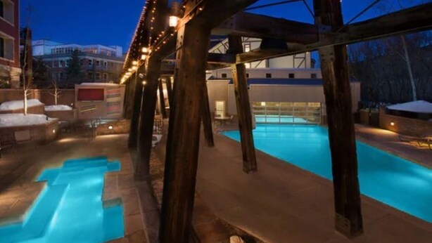 A swimming pool area with wooden beams and string lights, surrounded by stone steps and a covered seating area.