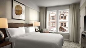 A hotel room with a large bed, two bedside tables with lamps, a framed artwork on the wall, a window with curtains, and a view of buildings outside.