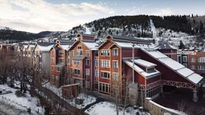 A multi-story hotel with a red and brown facade, set against a snowy mountain backdrop.