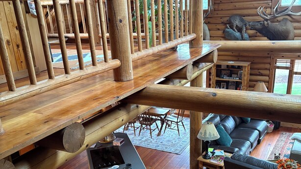 A rustic cabin interior with a wooden deck, a kitchen area with stools, a living room with a sofa, and a dining area. - Peaceful Log home on 9 mountainview acres (Molalla)
