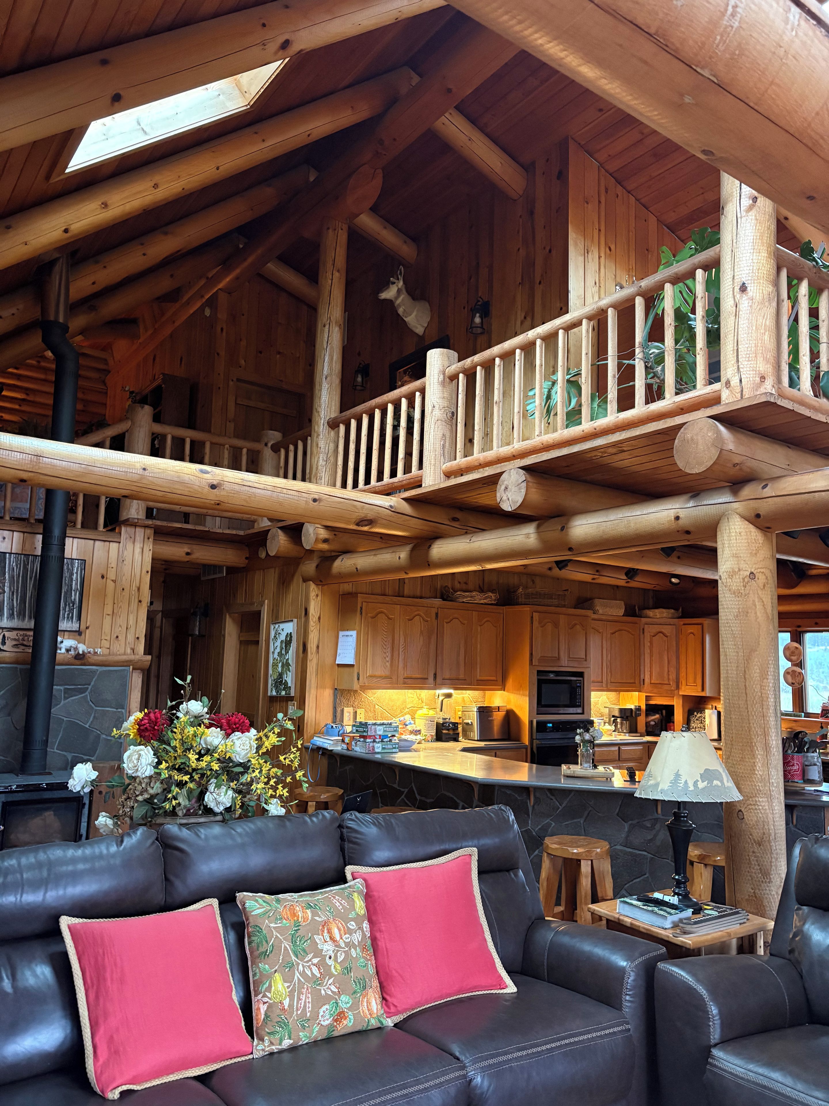 Amplia sala de estar con chimenea de piedra, balcón de madera y cocina al fondo.