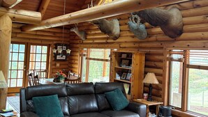 A log cabin interior with a leather sofa, a coffee table, and a dining area. - Peaceful Log home on 9 mountainview acres (Molalla)