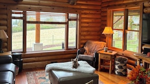 A log cabin interior with a leather sofa, a white furry ottoman, a wooden coffee table, and a television. - Peaceful Log home on 9 mountainview acres (Molalla)