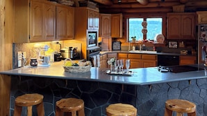 A rustic kitchen with wooden cabinetry, a large island with stools, and a stone countertop. - Peaceful Log home on 9 mountainview acres (Molalla)