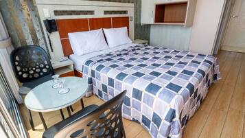 A hotel room with a bed, a desk with a chair, a small table, and a wardrobe.