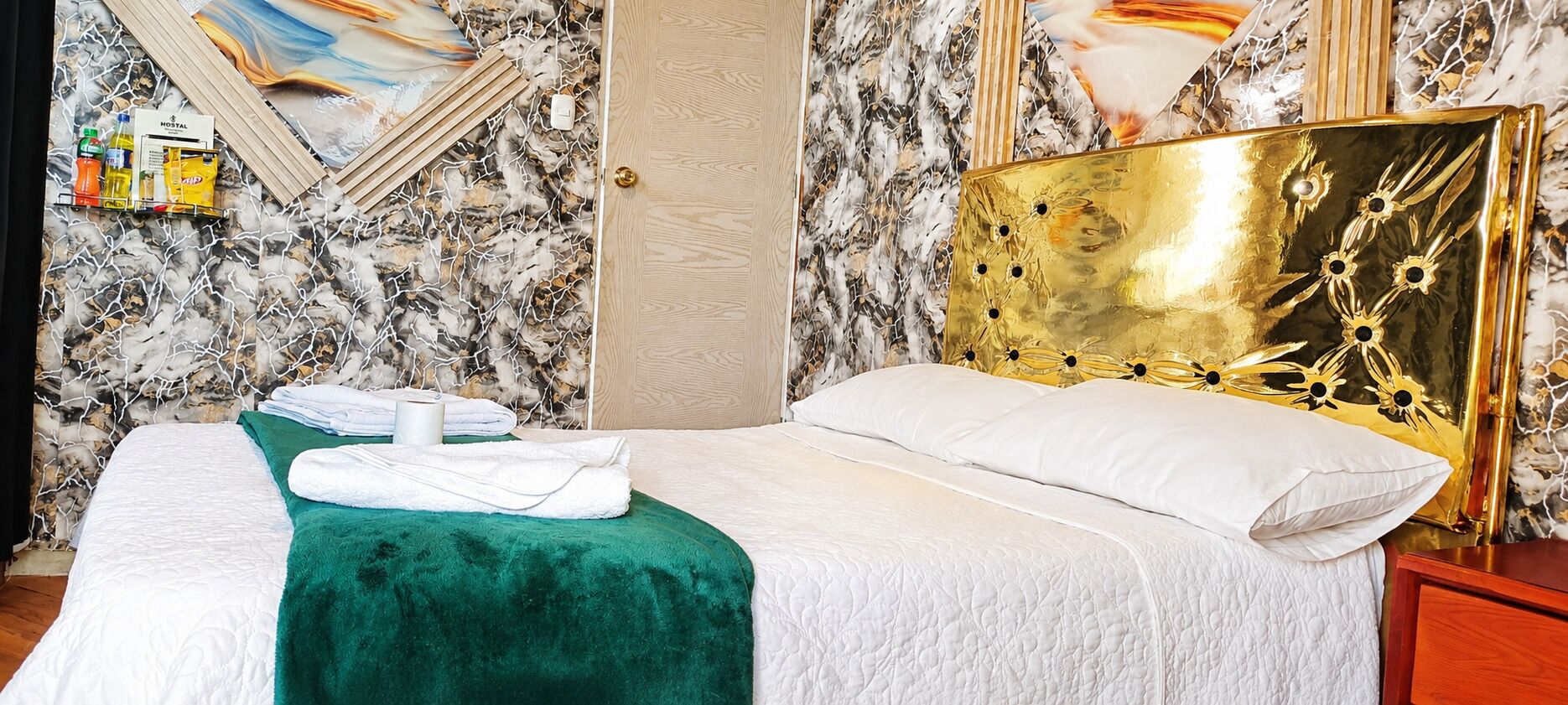 Habitación de hotel con cama, ropa de cama verde y blanca, cabecero dorado y pared con diseño de mármol.