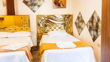 Habitación de hotel con dos camas, cada una con cabecero dorado, ropa de cama blanca y una toalla doblada sobre la cama.