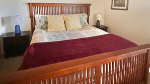 Un dormitorio con una cama de madera, un ventilador de techo, una mesita de noche y un cuadro enmarcado en la pared.