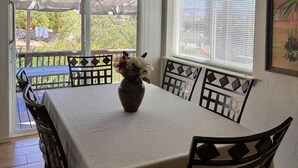 Un comedor con una mesa dispuesta para cuatro, un jarrón con flores y vistas a un patio con terraza de madera y vegetación.