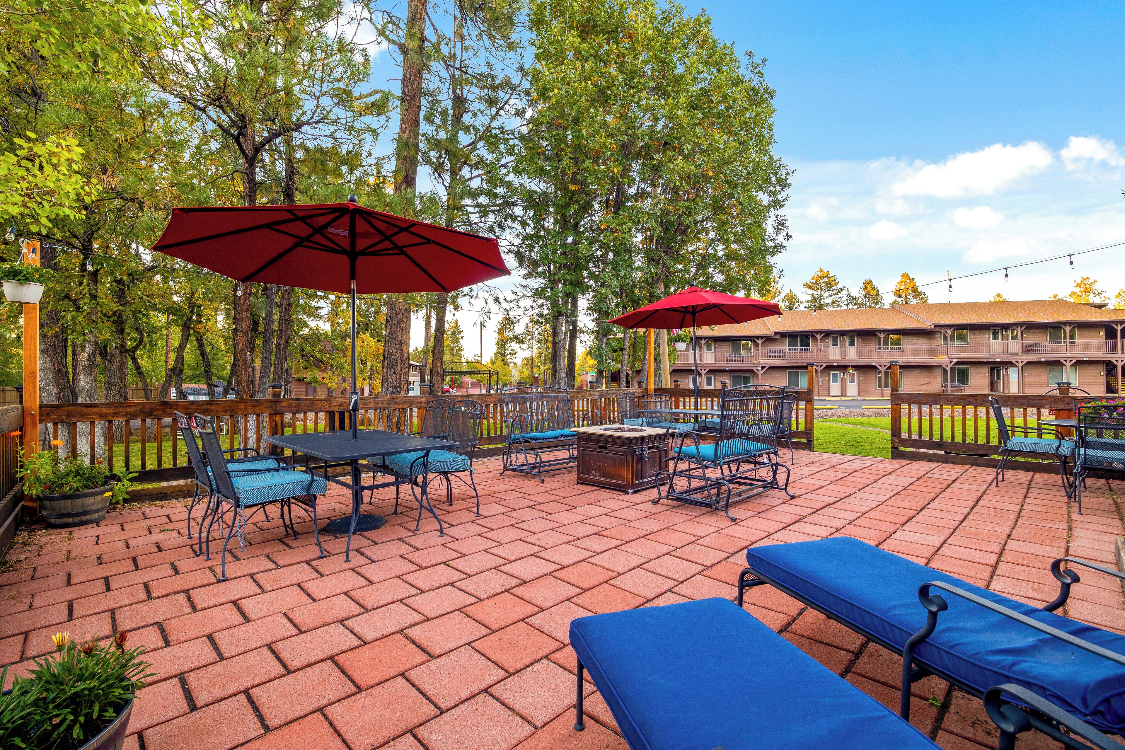 Un espace patio aménagé avec des meubles d’extérieur, notamment des tables et des chaises, ainsi que deux parasols rouges.