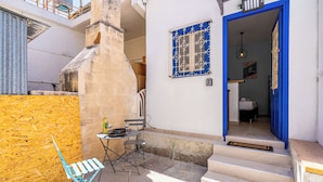 A small courtyard with a blue door leading to a bedroom, a table with a bottle and glasses, and a blue folding chair. - Simba Studio in Larnaca & Terrace (Larnaca)