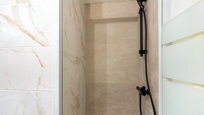 A shower area with beige tiles and a glass door. - Simba Studio in Larnaca & Terrace (Larnaca)