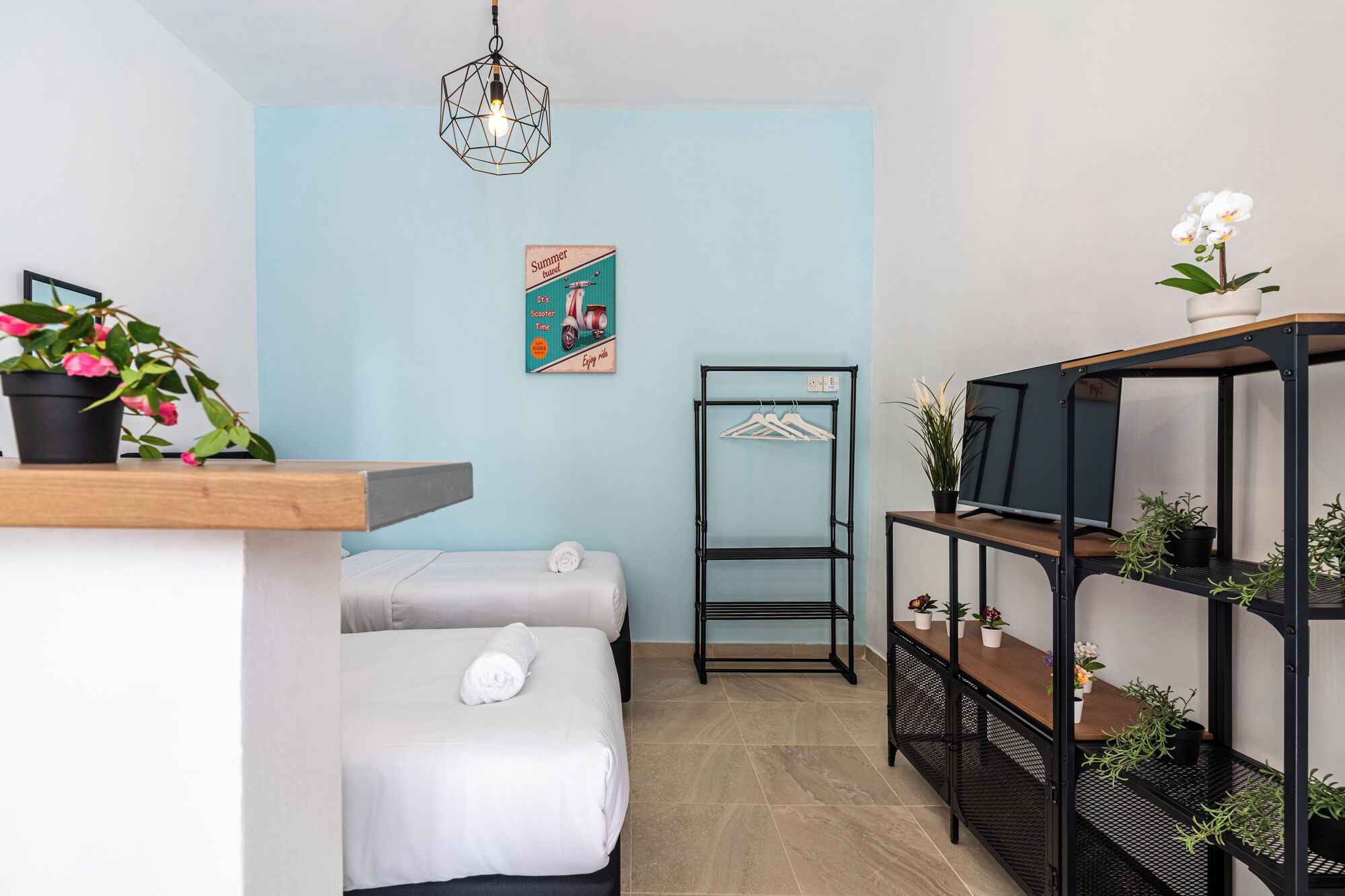 Un dormitorio con cama, lámpara colgante, televisor en la pared y estantería con plantas.