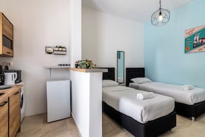 A compact hotel room with two single beds, a small kitchenette, a washing machine, and a mirror.