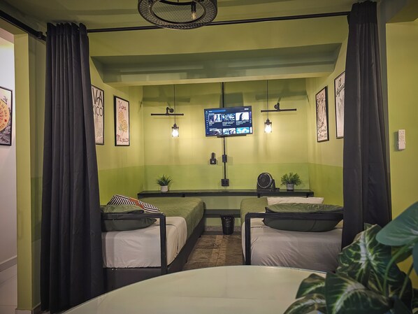 Ein Zimmer mit zwei Betten, einem an der Wand montierten Fernseher und einem kleinen Tisch mit einer Pflanze.