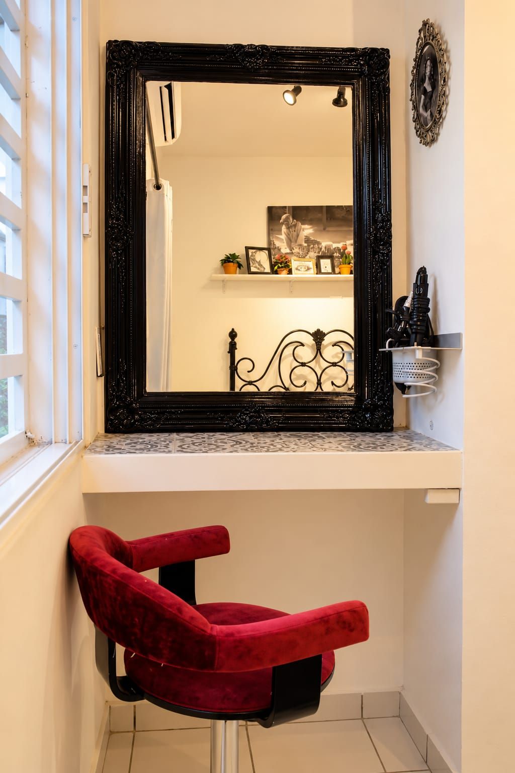 A bathroom with a large mirror, a red chair, and a shelf with various items.