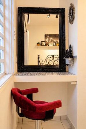 A bathroom with a large mirror, a red chair, and a shelf with various items.